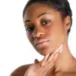 Une femme aux cheveux courts touche son menton, regardant pensivement la caméra sur un fond blanc uni. Réalisez ce look avec Univers Cosmetix, disponible pas cher au Sénégal.