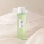 Un flacon vert de Beauty of Joseon Green Plum Tonique Rafraîchissant Hydratant, Resserre les Pores AHA + BHA 150 ml avec un bouchon blanc, présenté sur un fond en tissu doux et clair. dakar, Sénégal