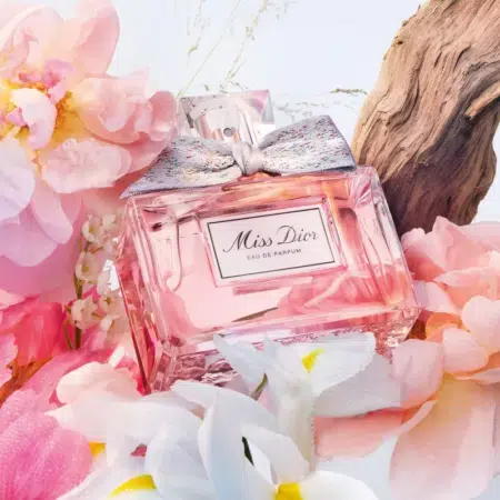 Un flacon DIOR J'adore Eau de Parfum pour femme 30 ml, entouré de fleurs roses et blanches et d'un morceau de bois flotté, rappelant l'élégance que l'on retrouve dans Miss Dior Eau de Parfum.