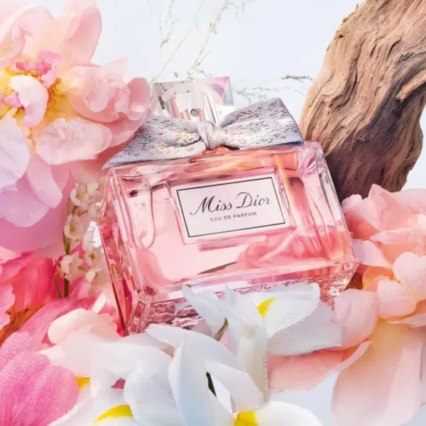 Un flacon DIOR J'adore Eau de Parfum pour femme 30 ml, entouré de fleurs roses et blanches et d'un morceau de bois flotté, rappelant l'élégance que l'on retrouve dans Miss Dior Eau de Parfum.