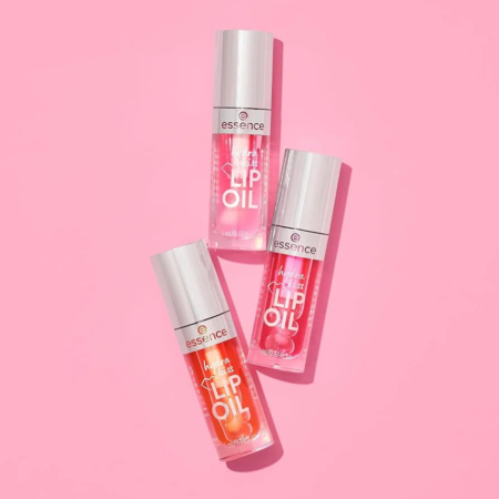 Trois flacons d'Huile à Lèvres Hydra Kiss 4 ml d'Essence Cosmetics colorés disposés sur un fond rose.