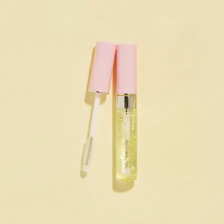 Tube de gloss transparent au capuchon rose, ouvert avec la tige applicatrice posée en diagonale sur un fond crème, rappelant le packaging épuré d'Etude My Lash Sérum pour Cils 9 g.