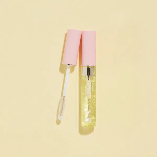 Tube de gloss transparent au capuchon rose, ouvert avec la tige applicatrice posée en diagonale sur un fond crème, rappelant le packaging épuré d'Etude My Lash Sérum pour Cils 9 g.