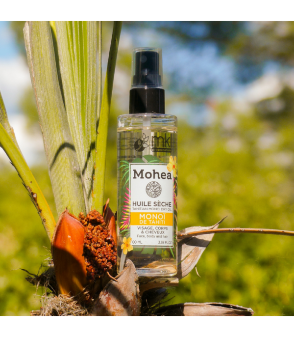 Un flacon de MKL Huile sèche - Monoï - 100 ml est niché au milieu d'un feuillage tropical avec un fond naturel flou, complété par les luxueux soins principaux MKL Crème pour une expérience de soin tropicale complète.