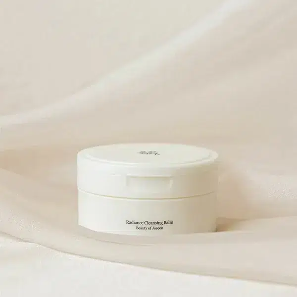 Un récipient blanc étiqueté « Beauty Of Joseon Radiance Baume Nettoyant Hydratant et Illuminateur 80g » repose sur un fond en tissu clair. dakar