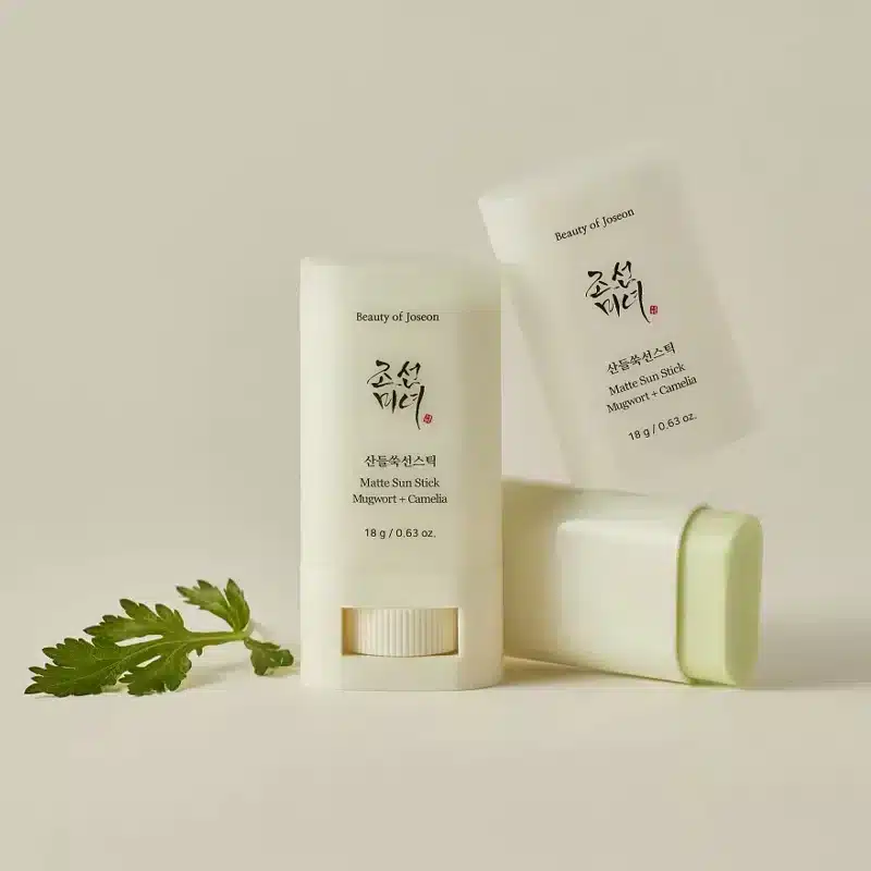 Deux tubes de Beauty of Joseon Matte Sun Stick Matifiant et Hydratant Spf50 18 g. Une feuille verte trône à côté d'eux