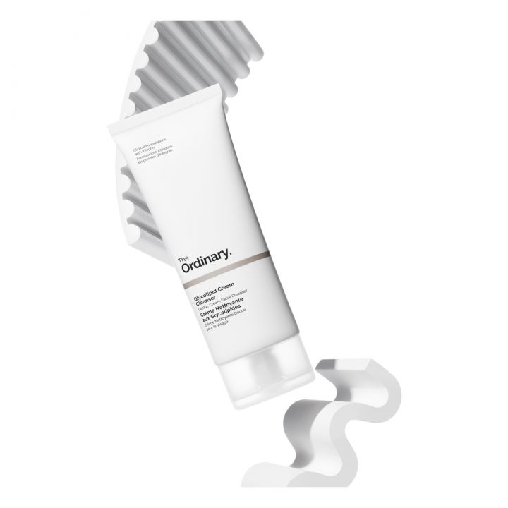 Un tube de The Ordinary Crème Démaquillante et Nettoyante aux Glycolipides 150 ml posé sur un fond blanc et ondulé respire la qualité.