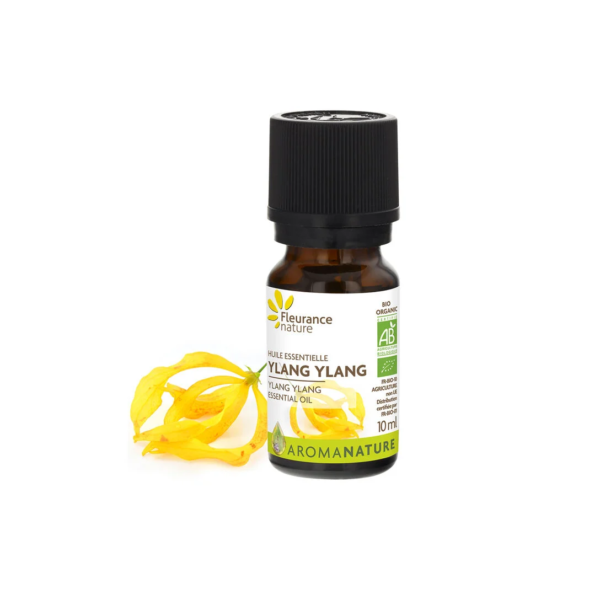 Un petit flacon de Fleurance Nature Huile Essentielle d'Ylang ylang Bio 10 ml est placé à côté de fleurs d'Ylang Ylang jaune vif sur un fond blanc immaculé. dakar