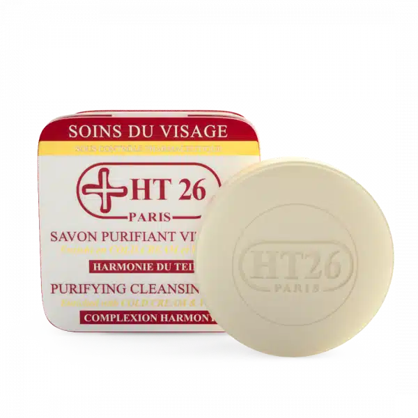 Un pain de savon rond étiqueté « HT 26 Paris » et « HT26 Savon Purifiant 150g » est placé devant sa boîte d'emballage avec un texte écrit en français et en anglais. dakar