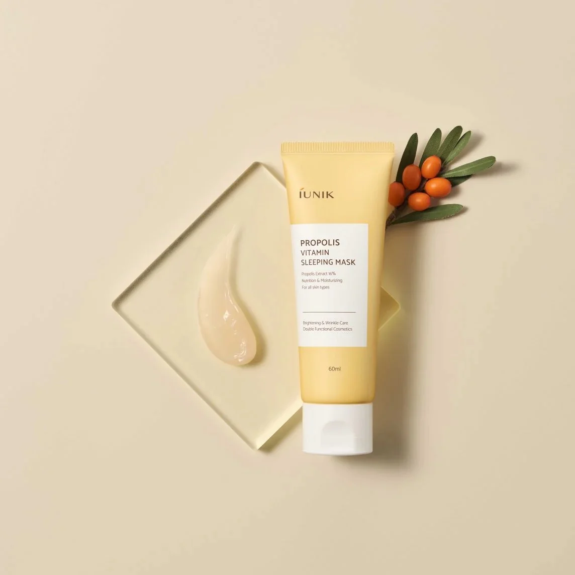 Un tube de IUnik Propolis Vitamin Masque de Nuit Rajeunissant et Éclaircissant 60 ml sur fond beige avec une trace du masque et quelques baies. dakar