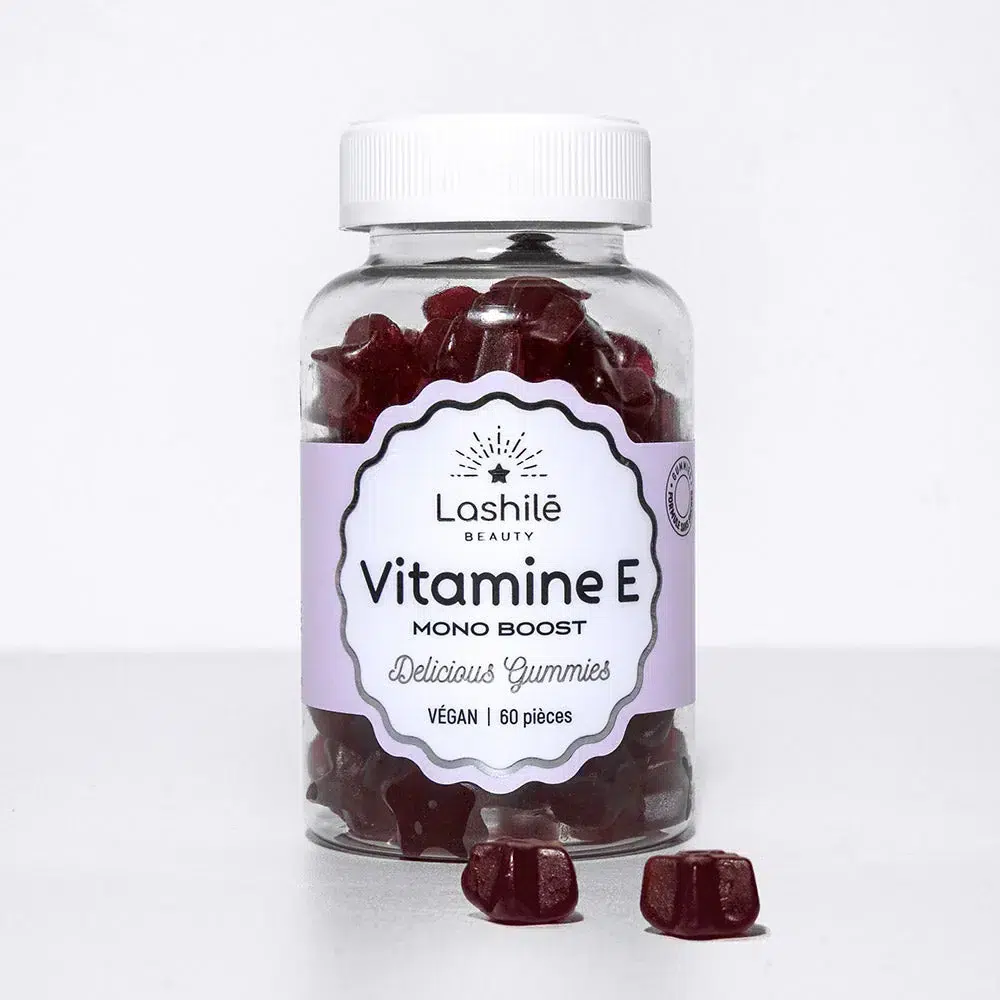 Une bouteille de gummies LASHILE BEAUTY Vitamine E Agit contre le stress oxydatif 60 pièces avec quelques-uns éparpillés devant. L'étiquette indique « 60 pièces