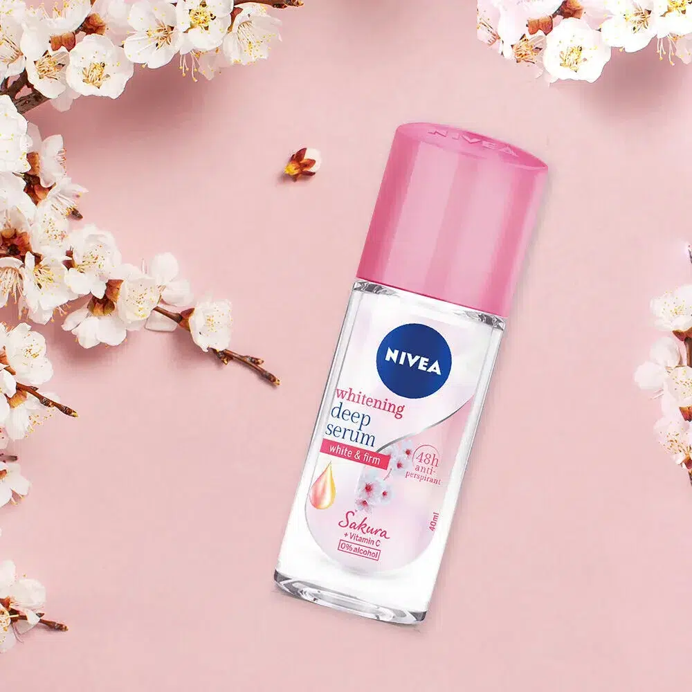 Nivea Brightening Deep Sakura + Vitamin C Serum Deodorant Éclaircissant Aisselles (40 ml) sur un fond rose avec des fleurs de cerisier entourant le flacon. dakar