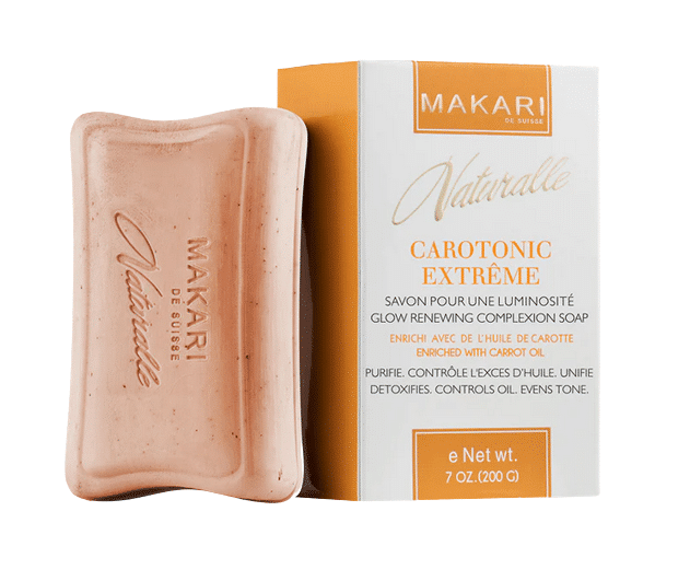 Pain de savon avec sa boîte. Le savon indique « Makari » et la boîte indique « Makari Naturalle Carotonic Extreme Savon Huile de Carotte 200g ». Coffret et savon sont beiges