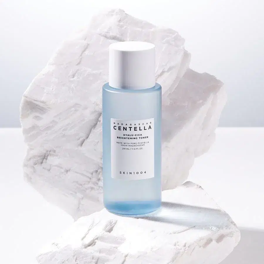 Un flacon bleu de SKIN1004 Madagascar Centella Tonique Éclat et Hydratant Acide Hyaluronique + Centella 210 ml posé sur des roches texturées blanches. dakar