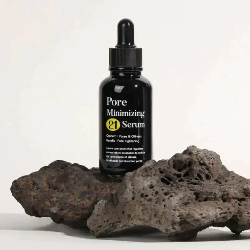 Un flacon de Tiam Sérum 21 Niacinamide Zinc Resserrement des Pores Et Clarifiant Teint 40 ml avec compte-gouttes est posé sur une roche volcanique rugueuse et sombre sur un fond uni. dakar