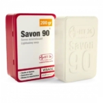 Un pain de savon éclaircissant Savon 90 est présenté à côté de son emballage rouge et blanc. L'emballage porte un texte indiquant qu'il clarifie, illumine et élimine les imperfections. Dakar