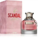 Un flacon de parfum Scandal, avec une base rose dégradée et un bouchon argenté, est présenté dans son coffret rose assorti. Le coffret porte l'inscription « SCANDAL » en lettres rouges et grasses. Le flacon est orné d'une petite breloque en forme de jambe. Dakar