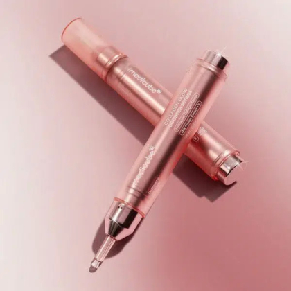 Deux tubes de soin or rose aux détails métalliques se croisent sur un fond rose tendre. Ils sont ornés d'un texte et d'un embout applicateur transparent, reflétant la lumière avec élégance. Dakar