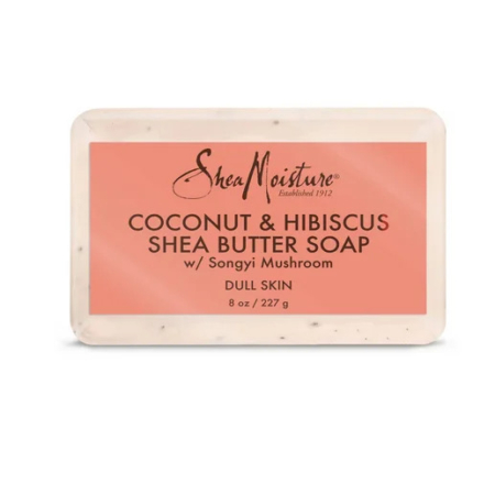 Pain de savon au beurre de karité SheaMoisture à la noix de coco et à l'hibiscus pour peaux ternes, 227 g. L'étiquette est rose avec un texte foncé détaillant des ingrédients comme le champignon Songyi. Le savon présente une texture légèrement blanc cassé. Dakar
